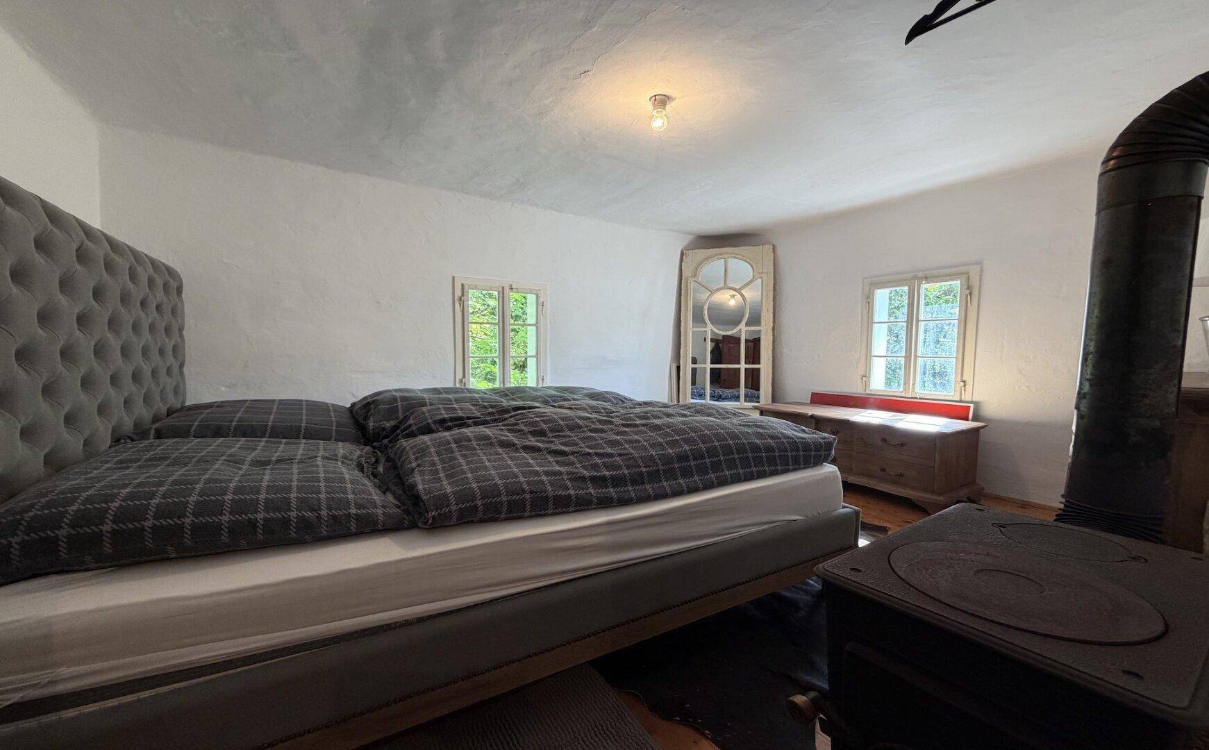 Rustikales Schlafzimmer mit großem Bett, Holzboden und traditionellem Ofen für Wärme.