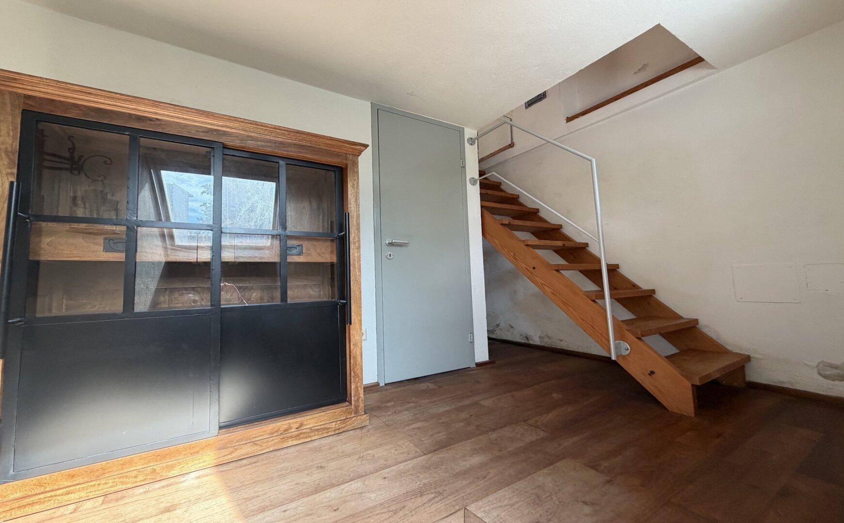 Raum mit Holztreppe, Holzboden und einem großen Schrank mit Glasfront.