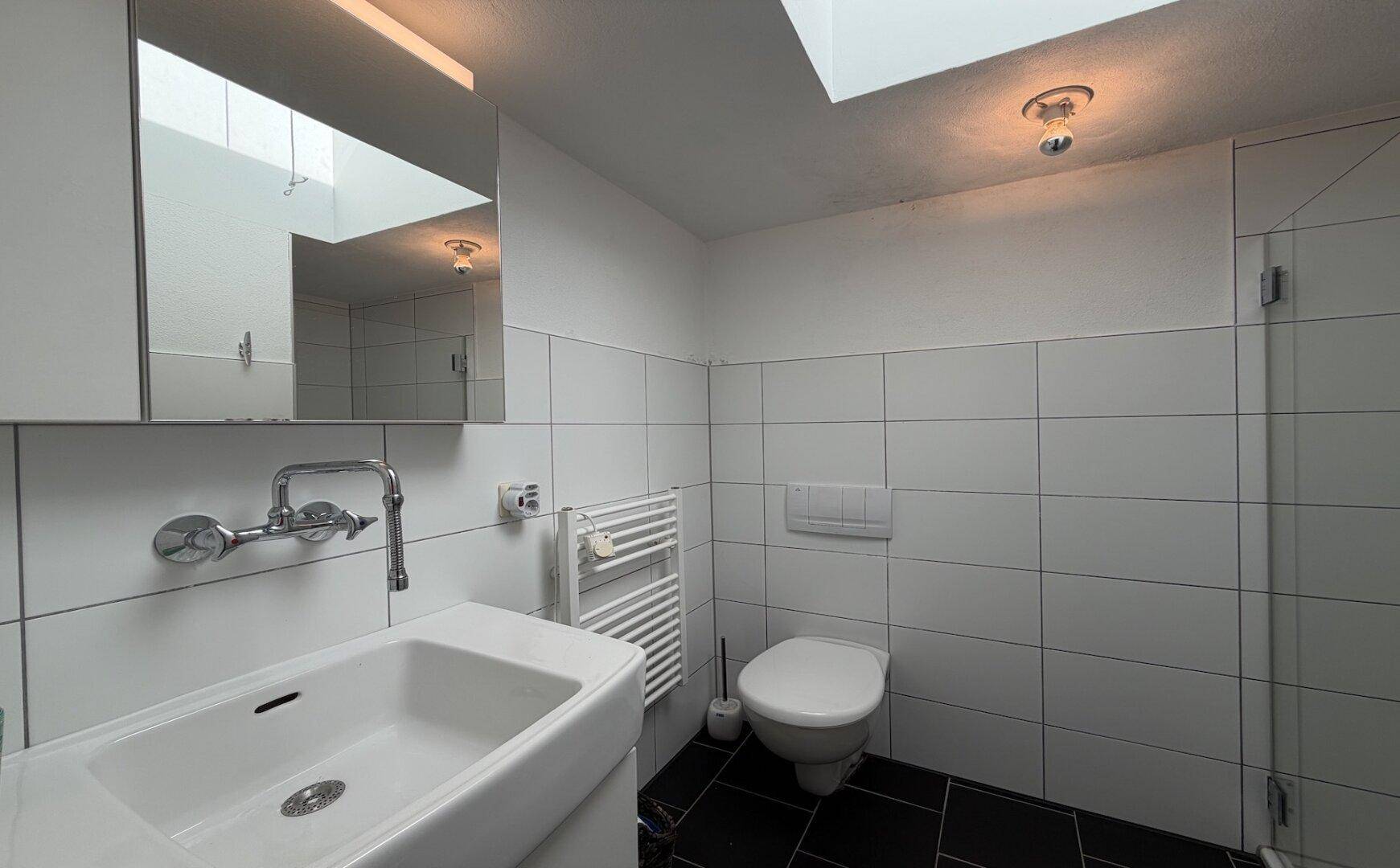 Modernes Badezimmer mit weißen Fliesen, schwarzem Boden und begehbarer Dusche.