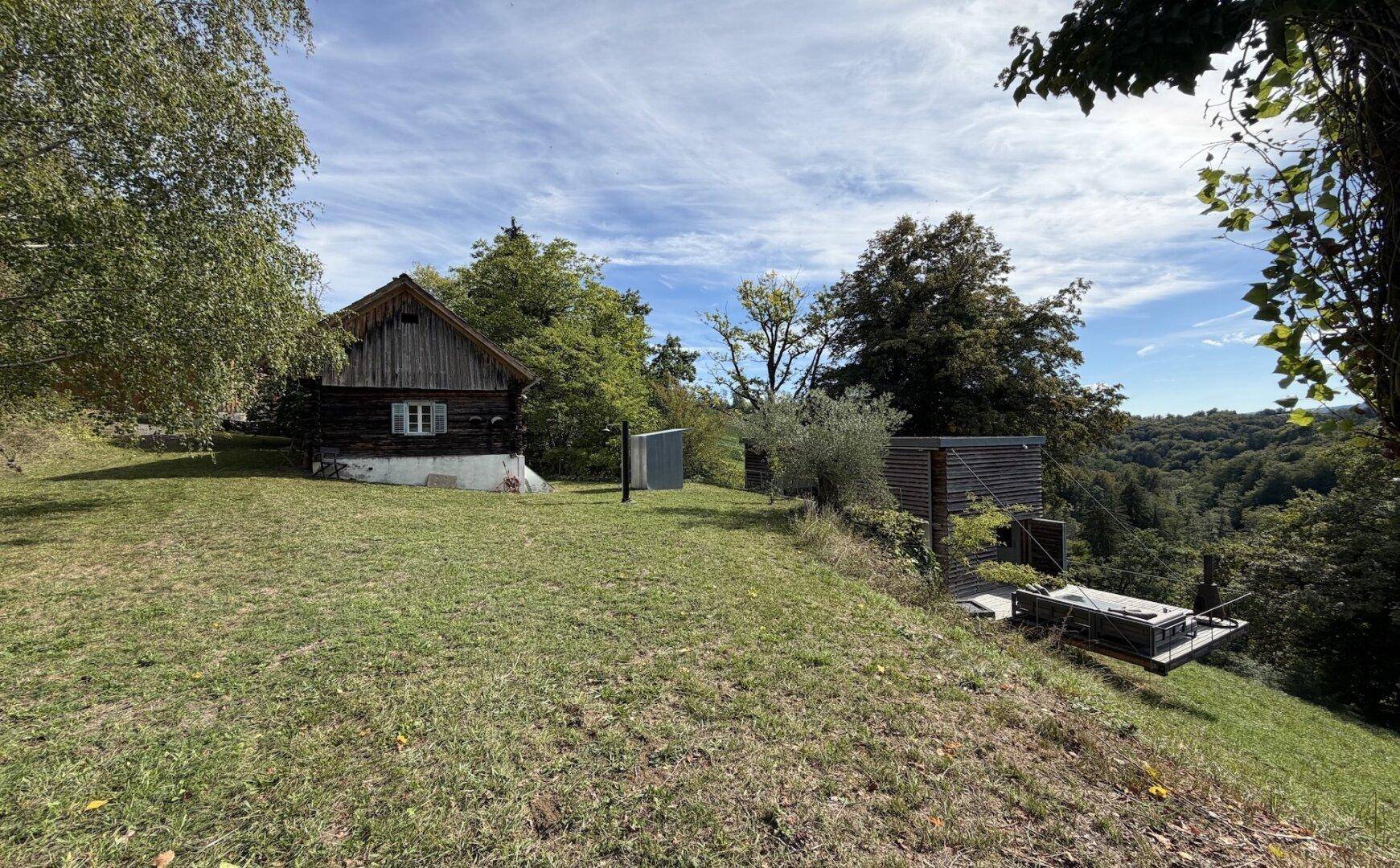 Panoramablick auf die beiden Häuser in einer idyllischen, grünen Hügellandschaft.