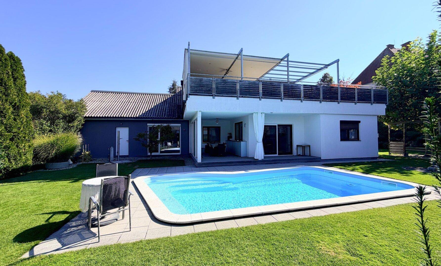 Gepflegter Garten mit rechteckigem Pool und angrenzender Terrasse unter blauem Himmel.