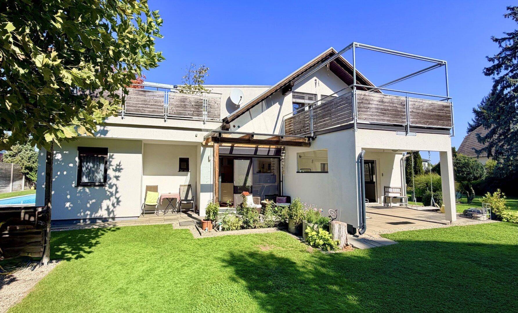 Seitlicher Blick auf das Haus mit Garten, bepflanzter Terrasse und Holzbalkonen.
