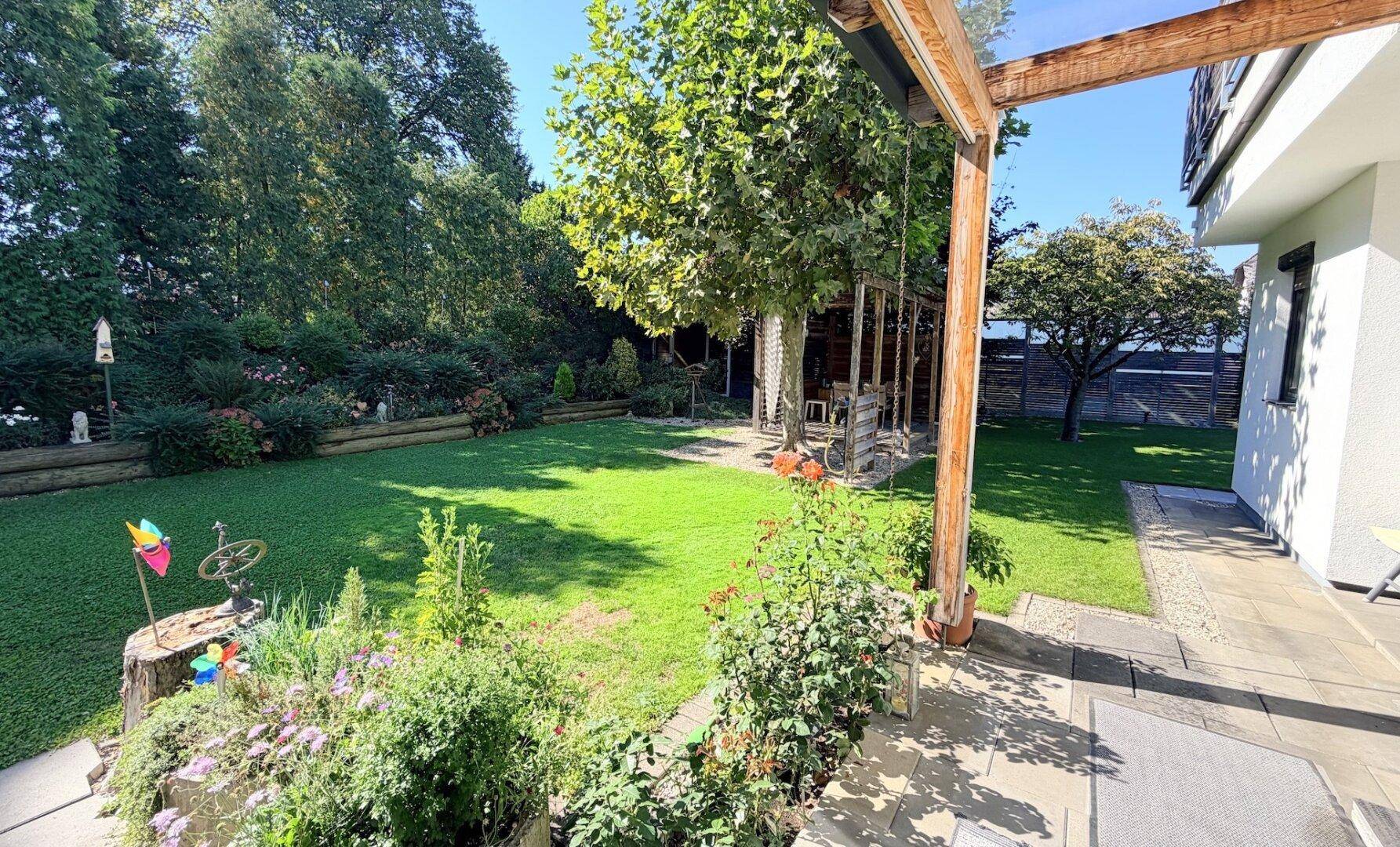 Weitläufiger Gartenbereich mit altem Baumbestand und sonnigen Rasenflächen.