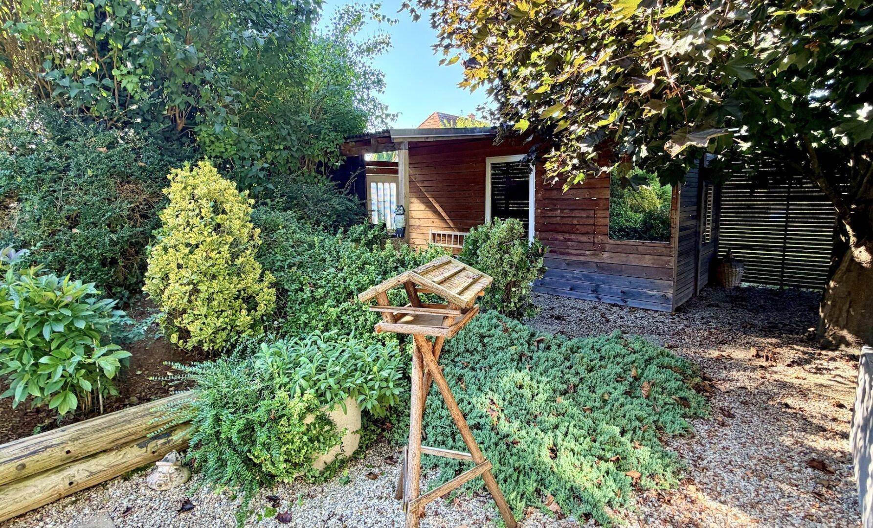 Idyllischer Gartenbereich mit Holzhütte und Vogelhäuschen, umgeben von üppigem Grün.