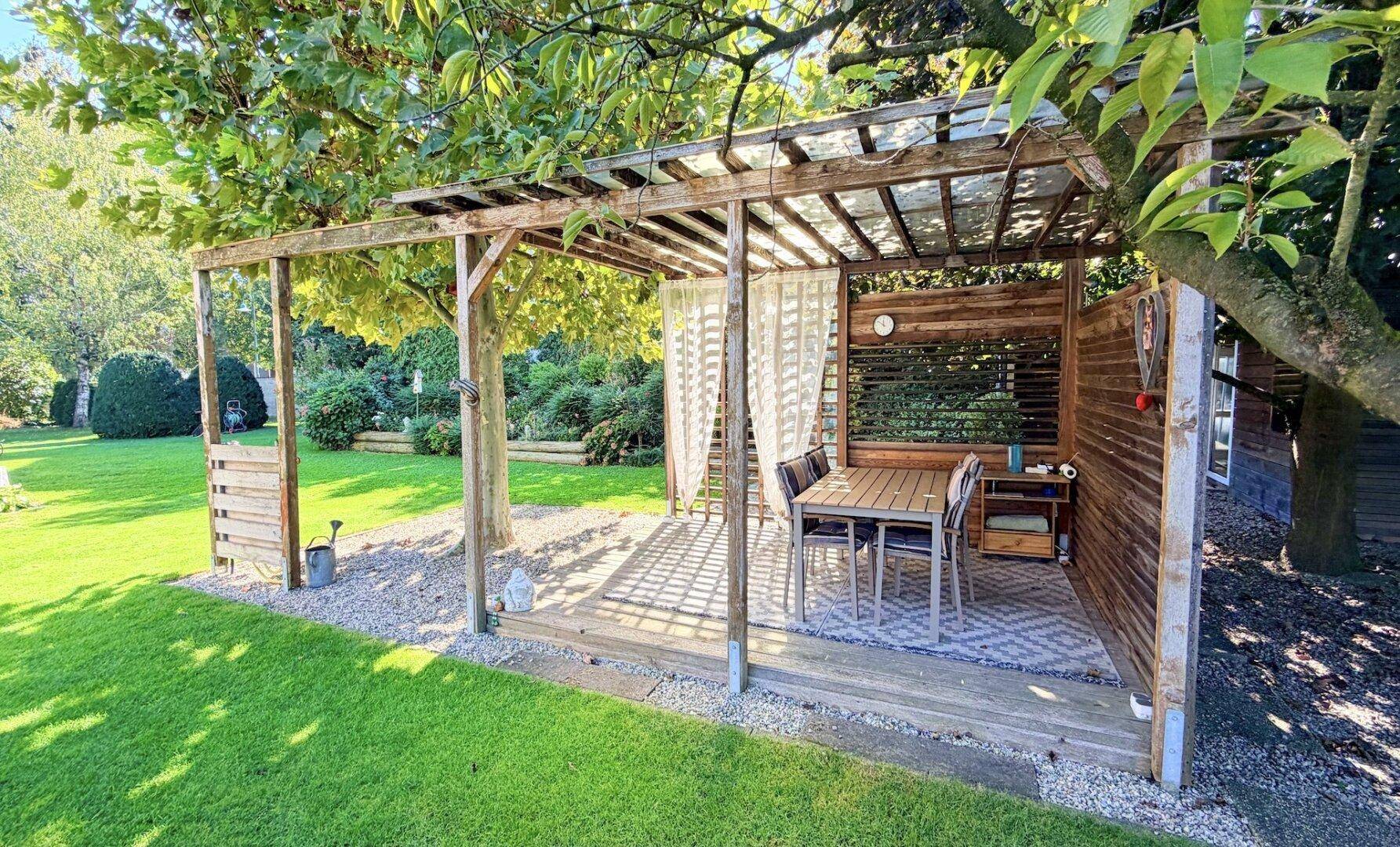 Überdachter Essbereich im Garten unter einer Holzpergola, ideal für Mahlzeiten im Freien.