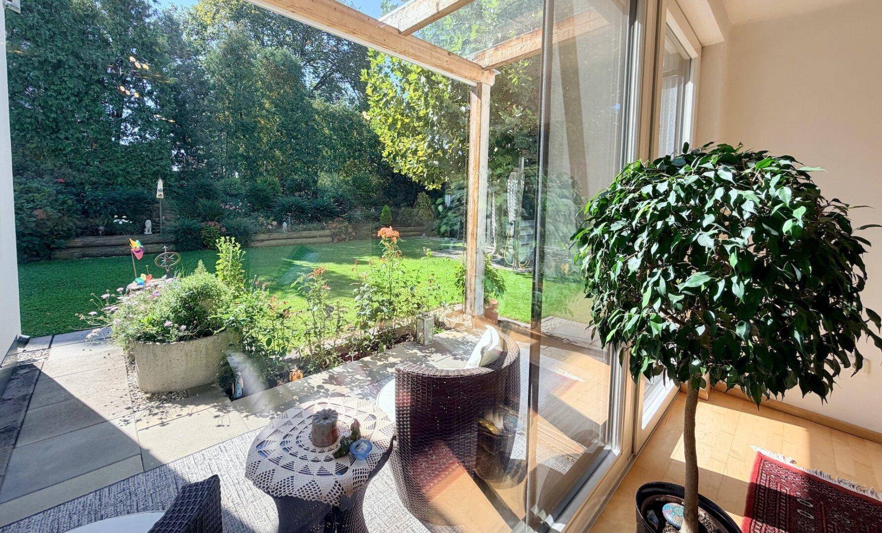Sonniger Terrassenbereich mit üppigen Pflanzen, direkt vom Wohnraum zugänglich.