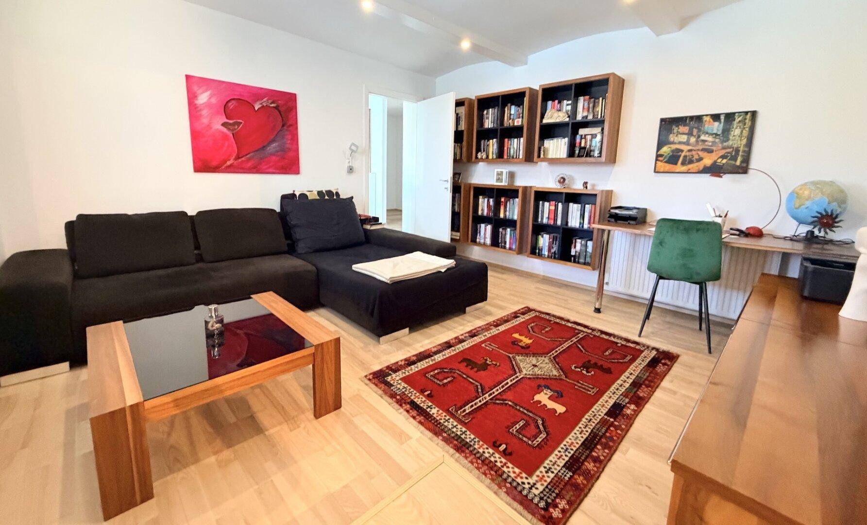 Gemütliches Wohnzimmer mit Sofa, Bücherregalen und Arbeitsbereich.