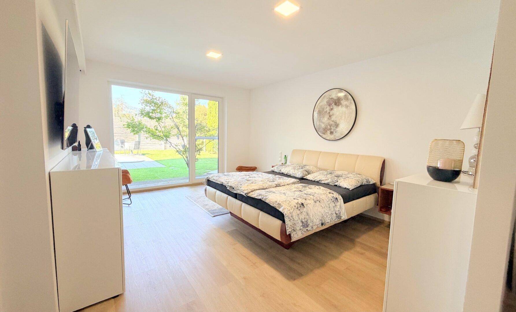 Geräumiges Schlafzimmer mit Doppelbett und großen Fenstern zum Garten.