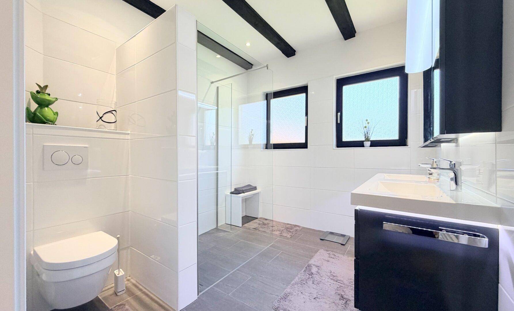 Helles Badezimmer mit begehbarer Dusche, Doppelwaschbecken und freiliegenden Holzbalken.