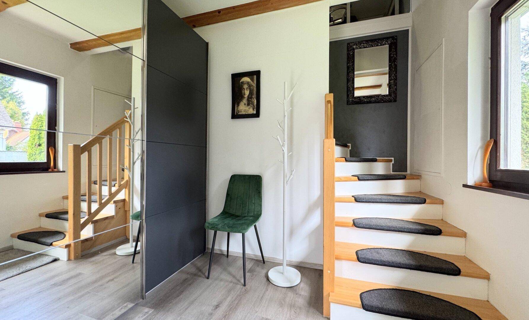 Heller Eingangsbereich mit Holztreppe, Spiegelwand und modernem Design unter sichtbaren Holzbalken.
