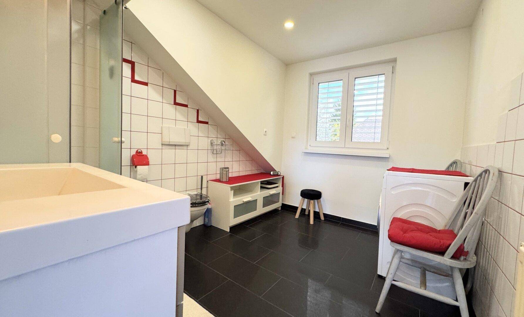 Funktionales Badezimmer mit Dusche, Waschmaschine und Fenster unter einer praktischen Dachschräge.