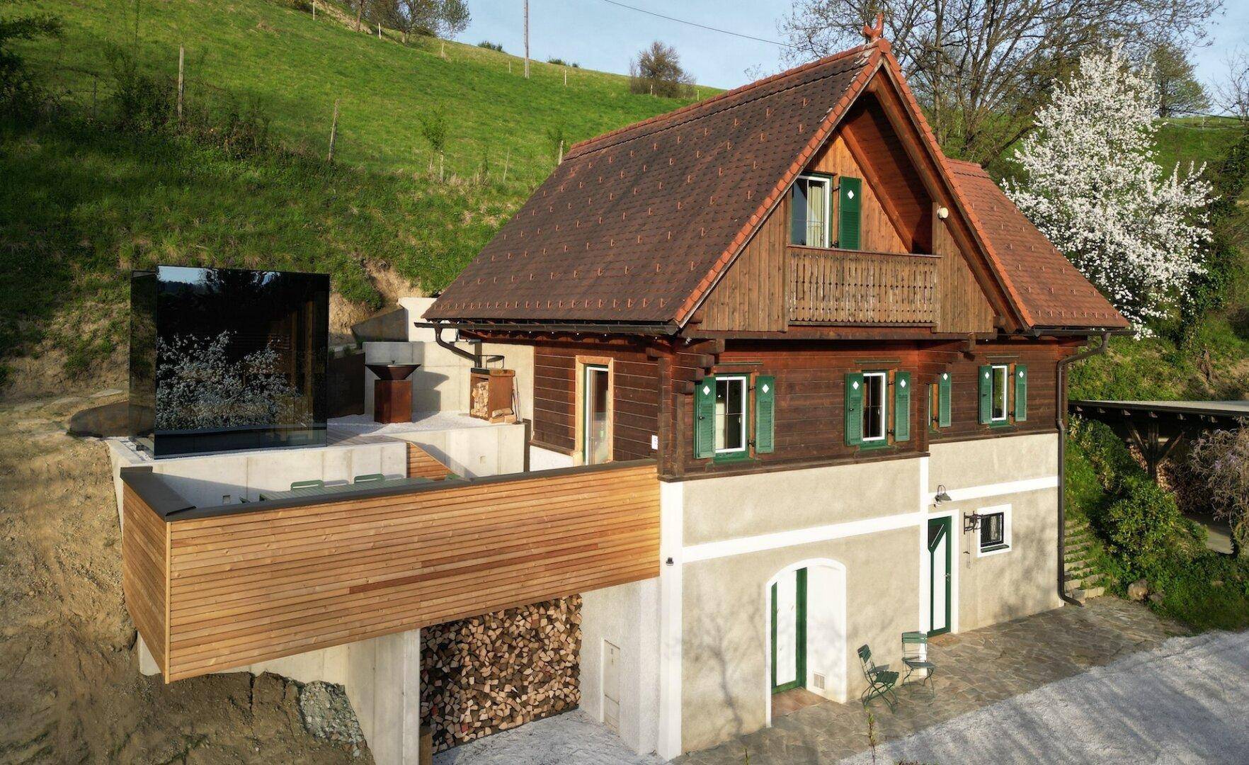 Modernisiertes Landhaus mit Holzfassade, neuer Terrasse und einem verspiegelten Anbau.