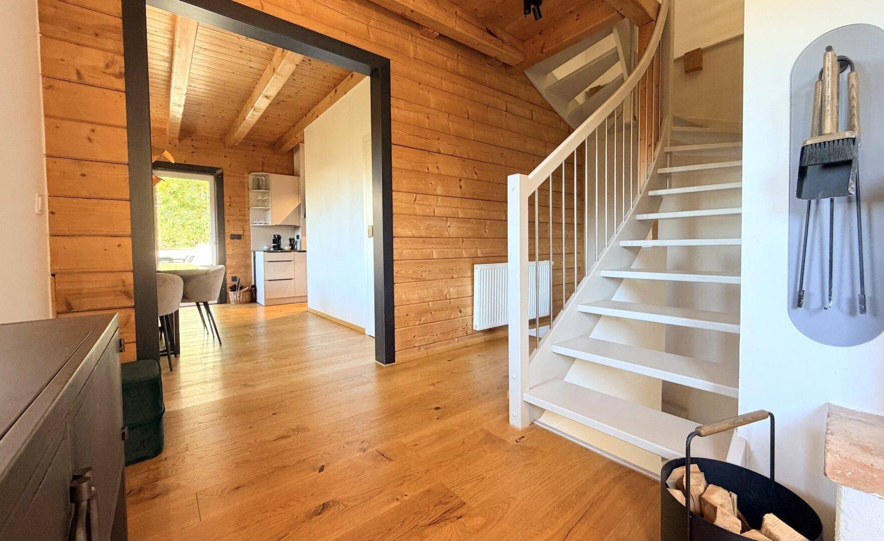 Heller Flur mit Holzvertäfelung, weißer Treppe und Zugang zur Küche.