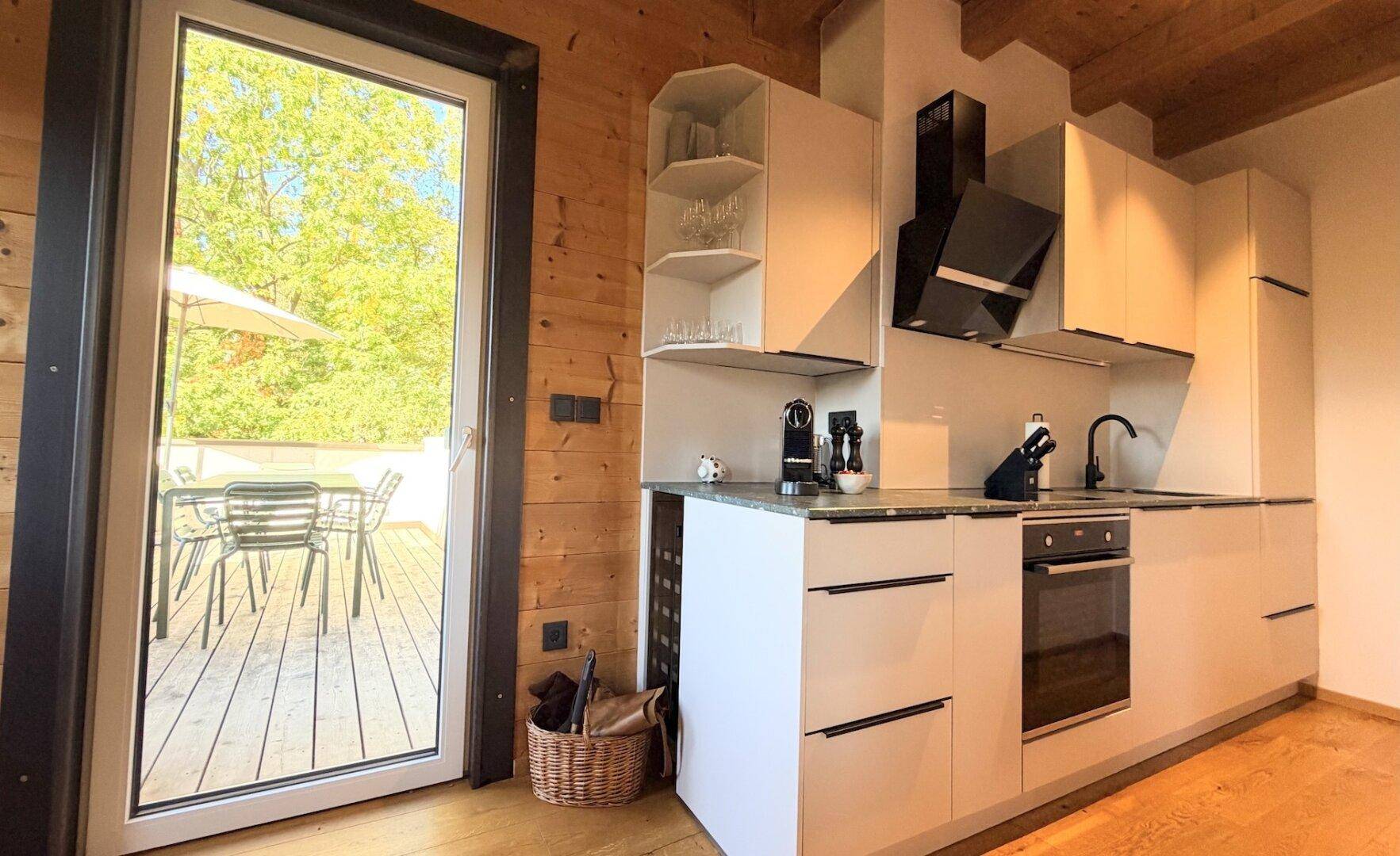 Moderne Küche mit weißen Schränken, integrierten Geräten und direktem Zugang zur Terrasse.