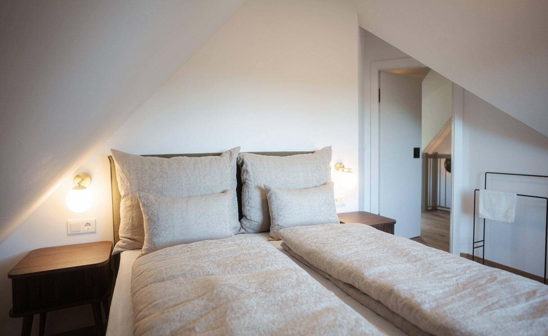 Komfortables Schlafzimmer mit weichen Textilien, Holzboden und indirekter Beleuchtung.