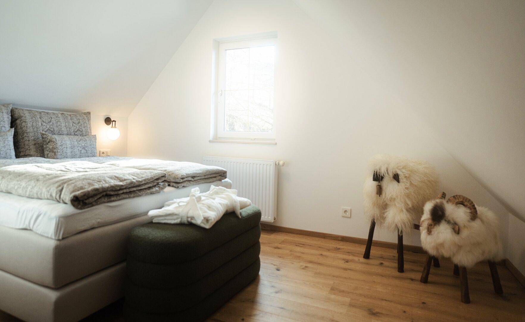 Helles Schlafzimmer mit Fenster, Holzboden und charmanten Dekorationselementen.