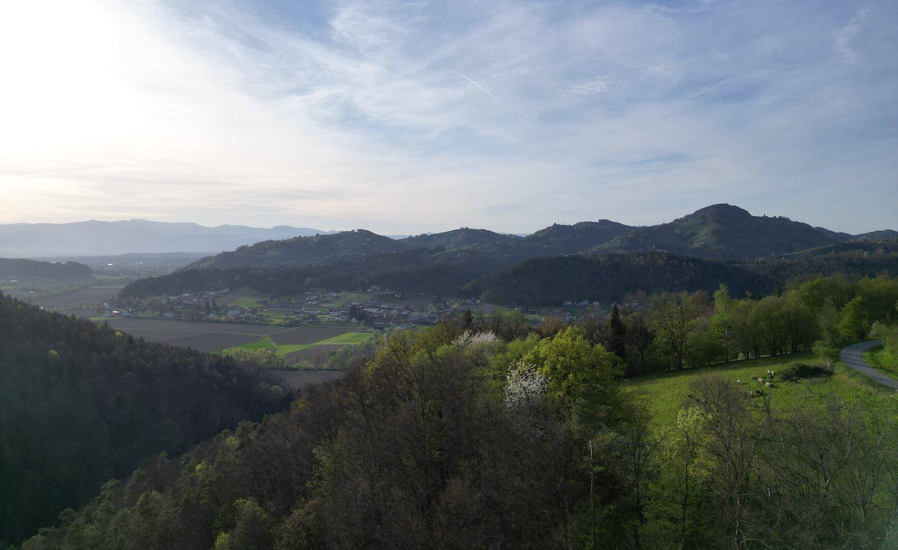 Weitläufiger Blick über die sanfte Hügellandschaft und ein kleines Dorf in der Ferne.