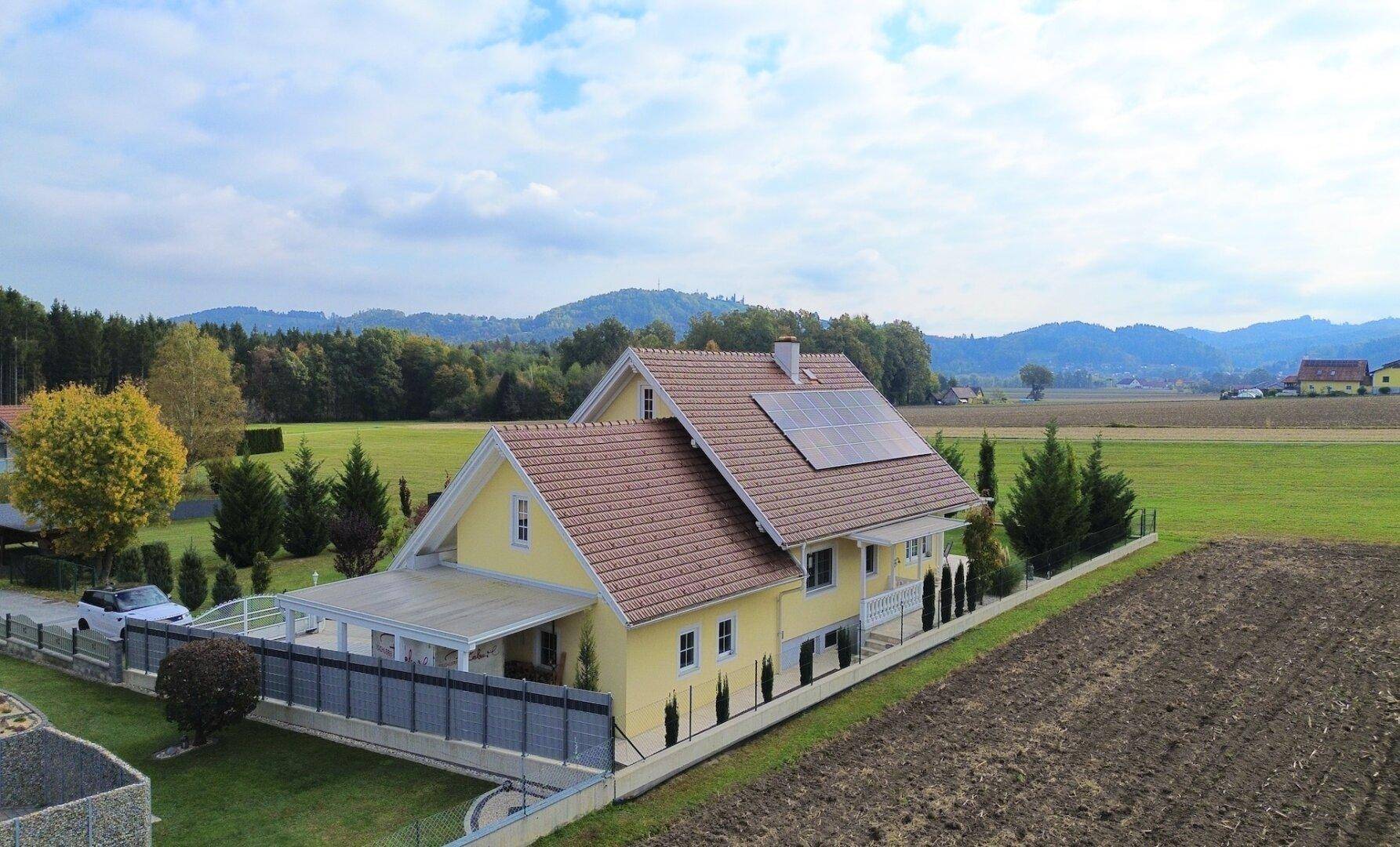 Luftaufnahme des Hauses mit Photovoltaikanlage und weitem Blick ins Grüne und auf Hügel.