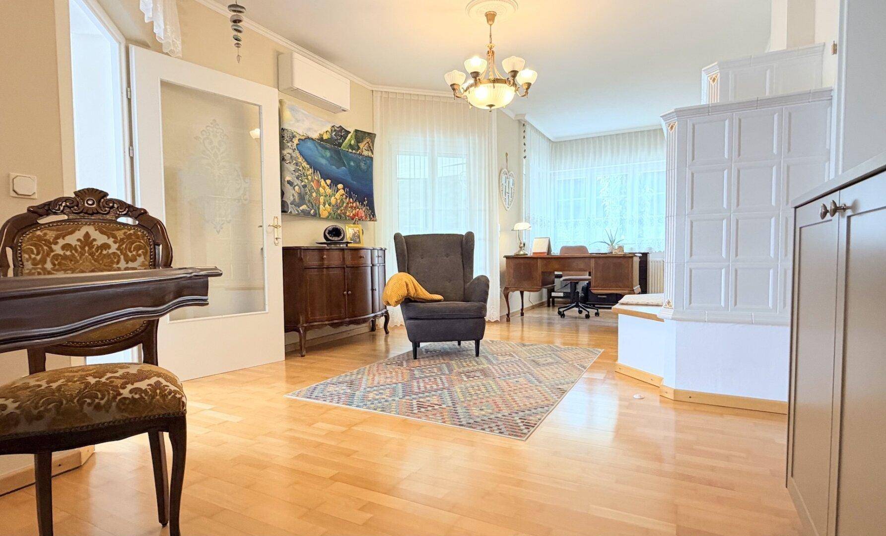 Helles Wohnzimmer mit Holzboden, Kachelofen und klassischer Möblierung, auch als Büro nutzbar.