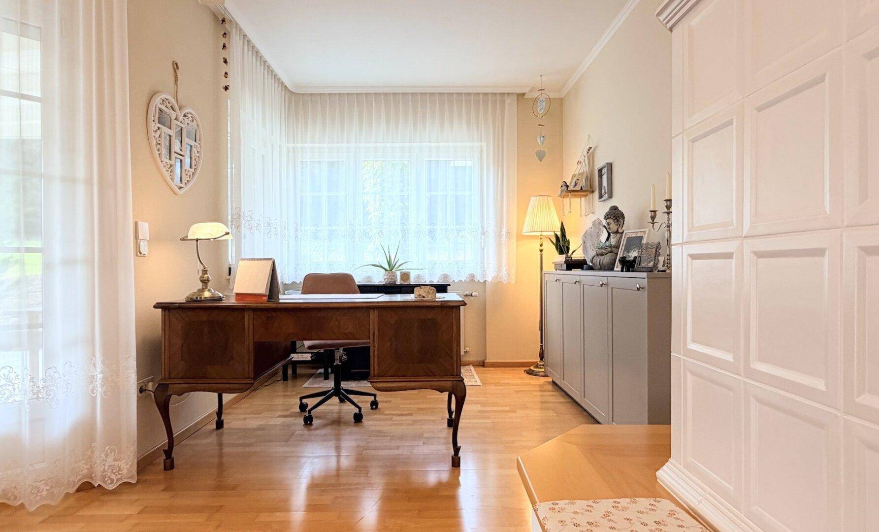Ruhiges Arbeitszimmer mit großem Schreibtisch, Holzboden und Blick ins Grüne durch das Fenster.