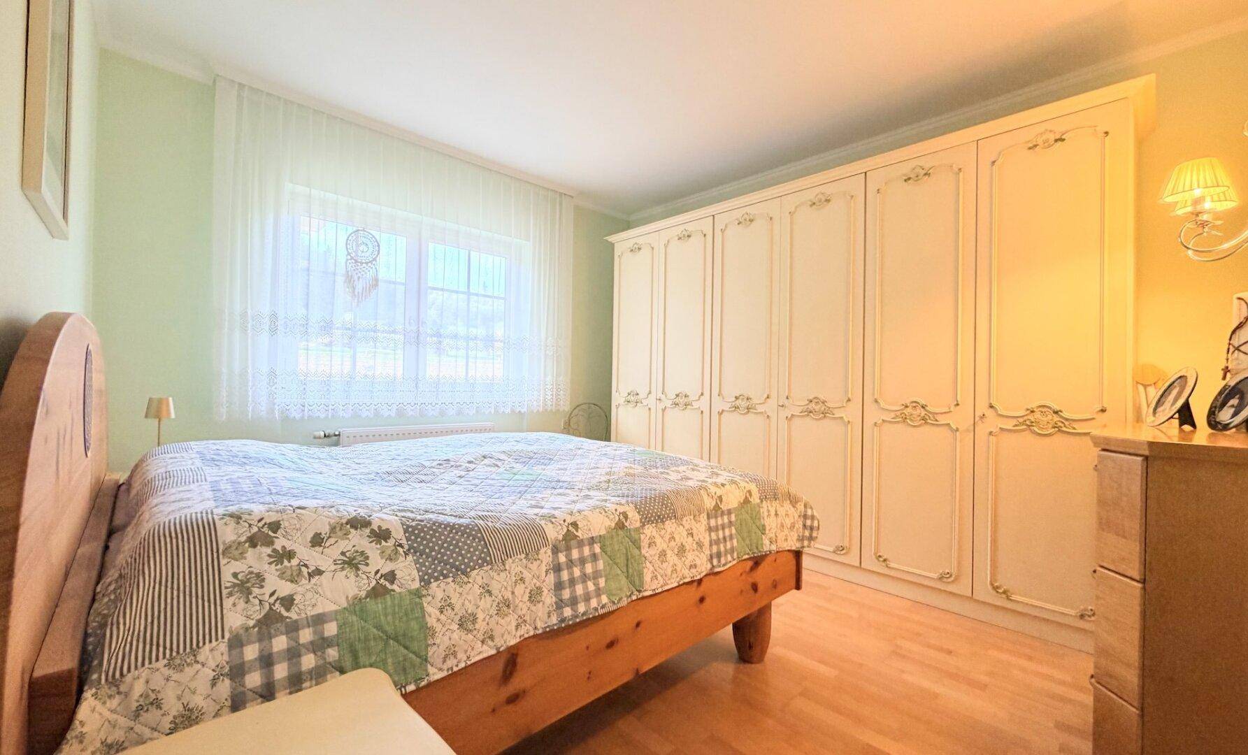 Geräumiges Schlafzimmer mit Holzbett, großem Kleiderschrank und hellem Ambiente, grüne Wände.
