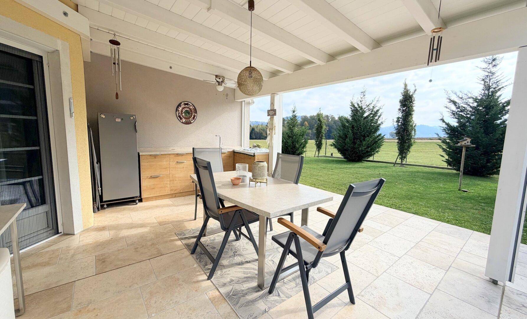 Überdachte Terrasse mit Essbereich im Freien und weitem Blick ins Grüne und auf Felder.