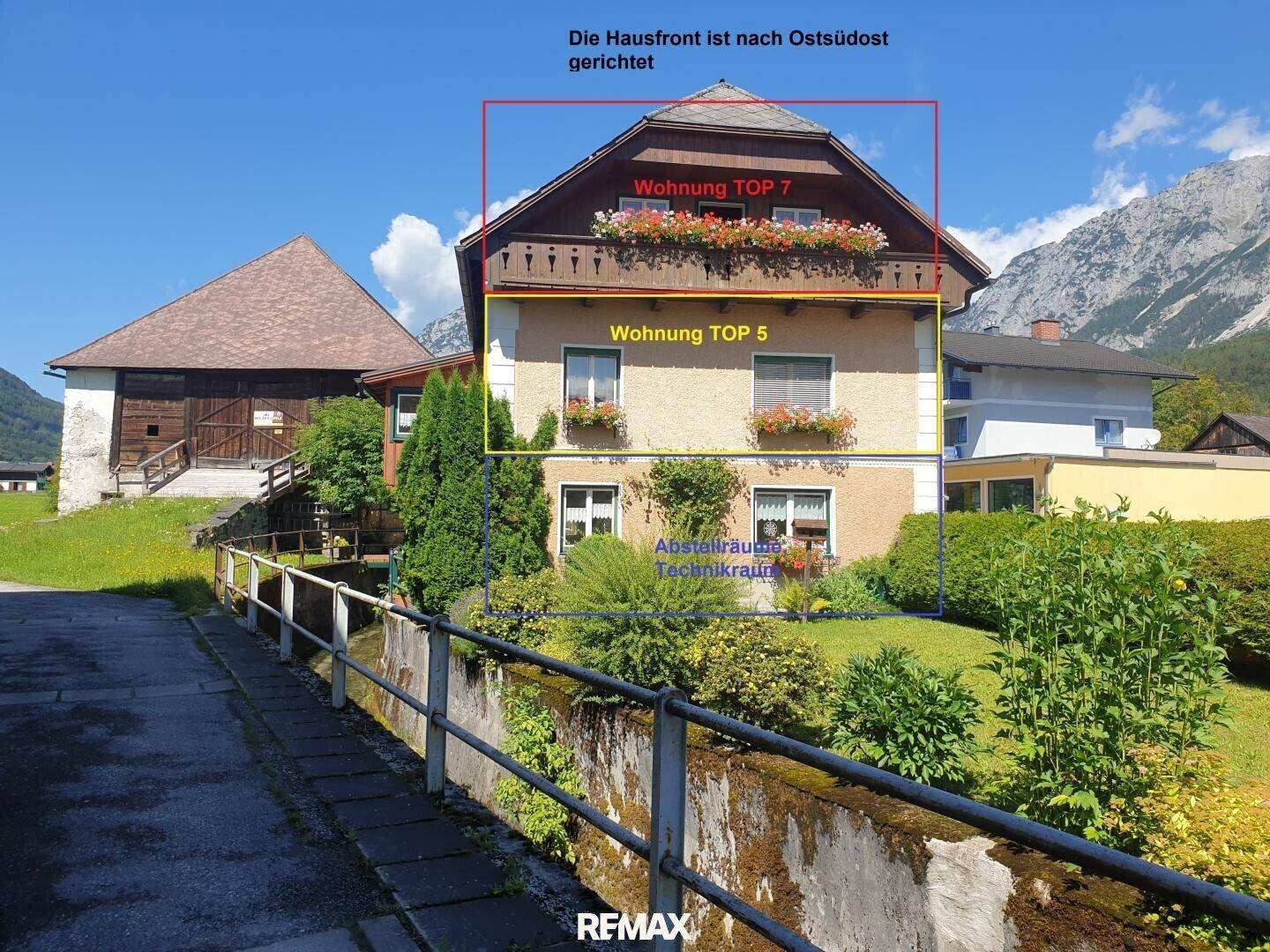 Gebäudeansicht mit markierten Wohneinheiten und einem gepflegten Gartenbereich im Vordergrund.