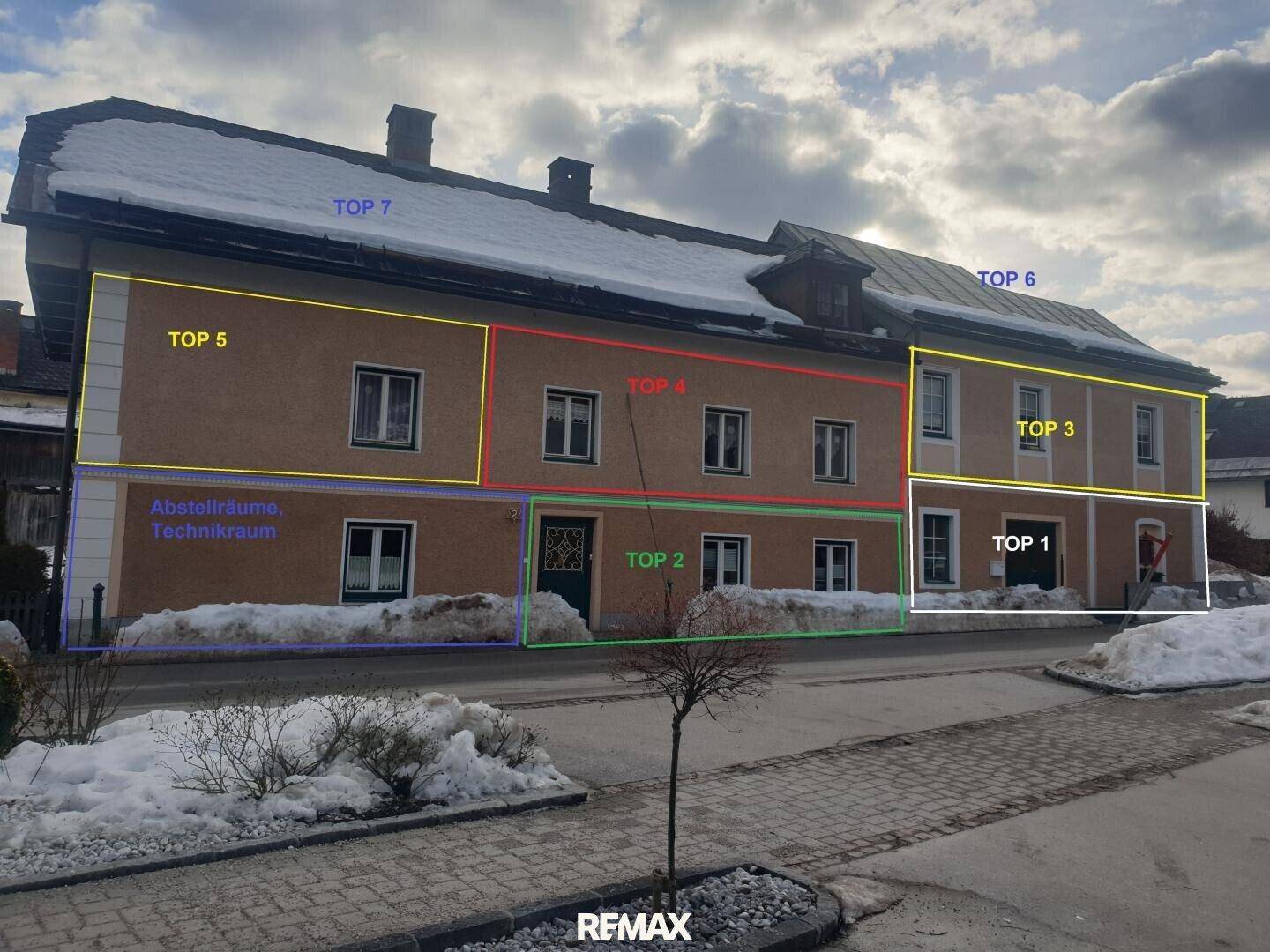 Gebäudefassade im Winter mit Schnee und markierten Bereichen für verschiedene Wohneinheiten.