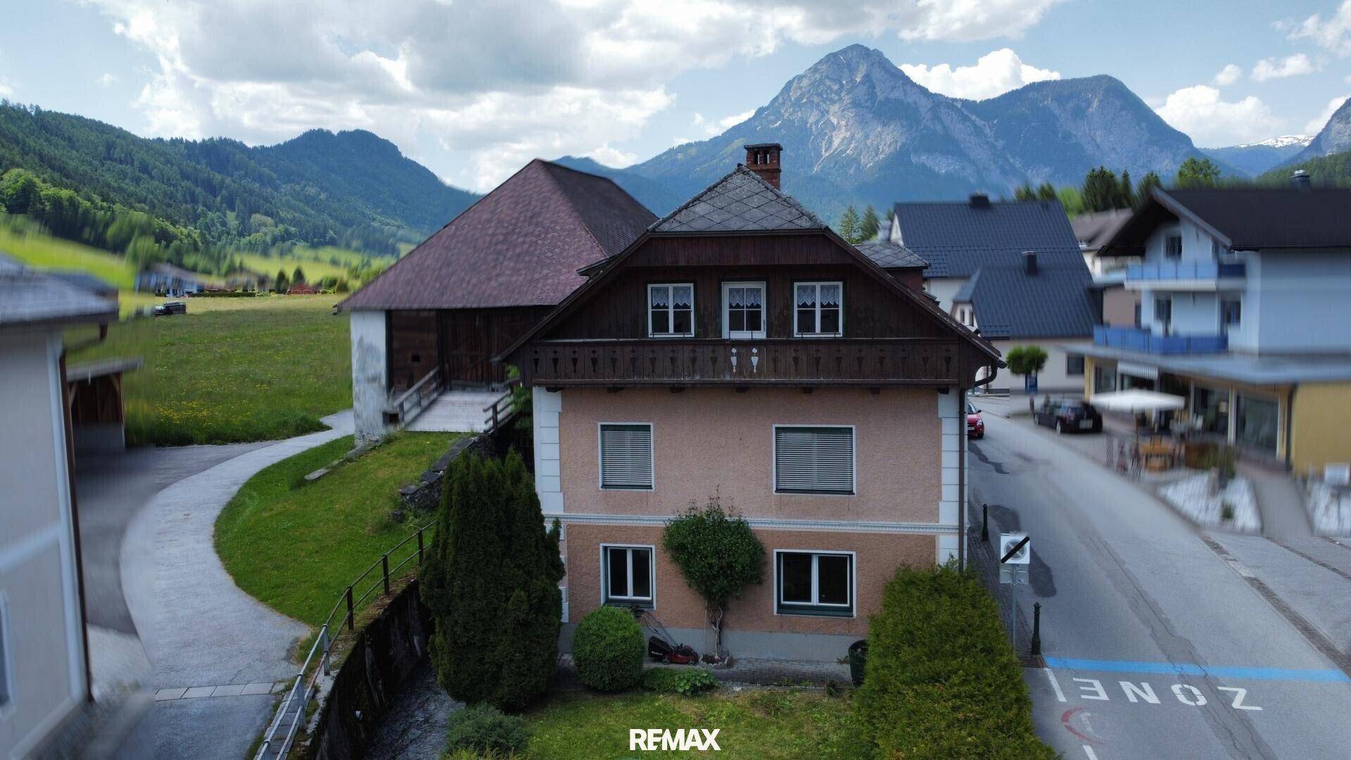 Gebäude mit traditioneller Architektur und kleinem Vorgarten vor einer beeindruckenden Bergkulisse.