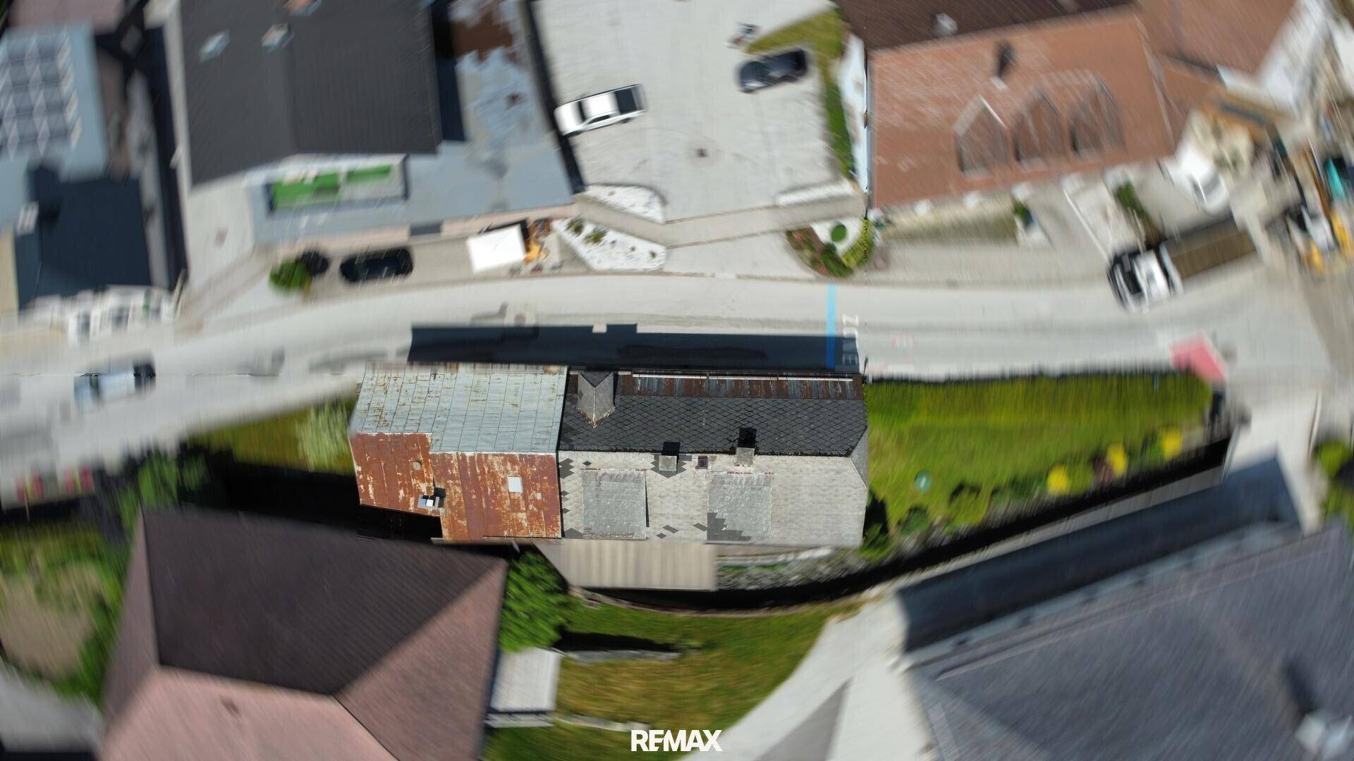 Luftaufnahme von oben zeigt Dächer von Gebäuden und eine Straße in einer ländlichen Umgebung.