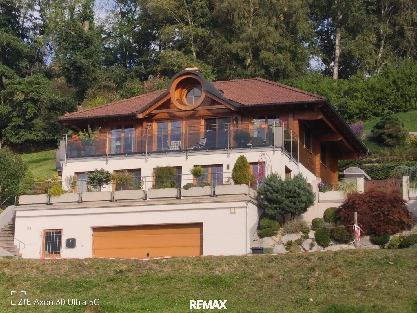 Charmantes Holzhaus mit mehreren Balkonen und integrierter Garage, eingebettet in eine grüne Hügellandschaft.
