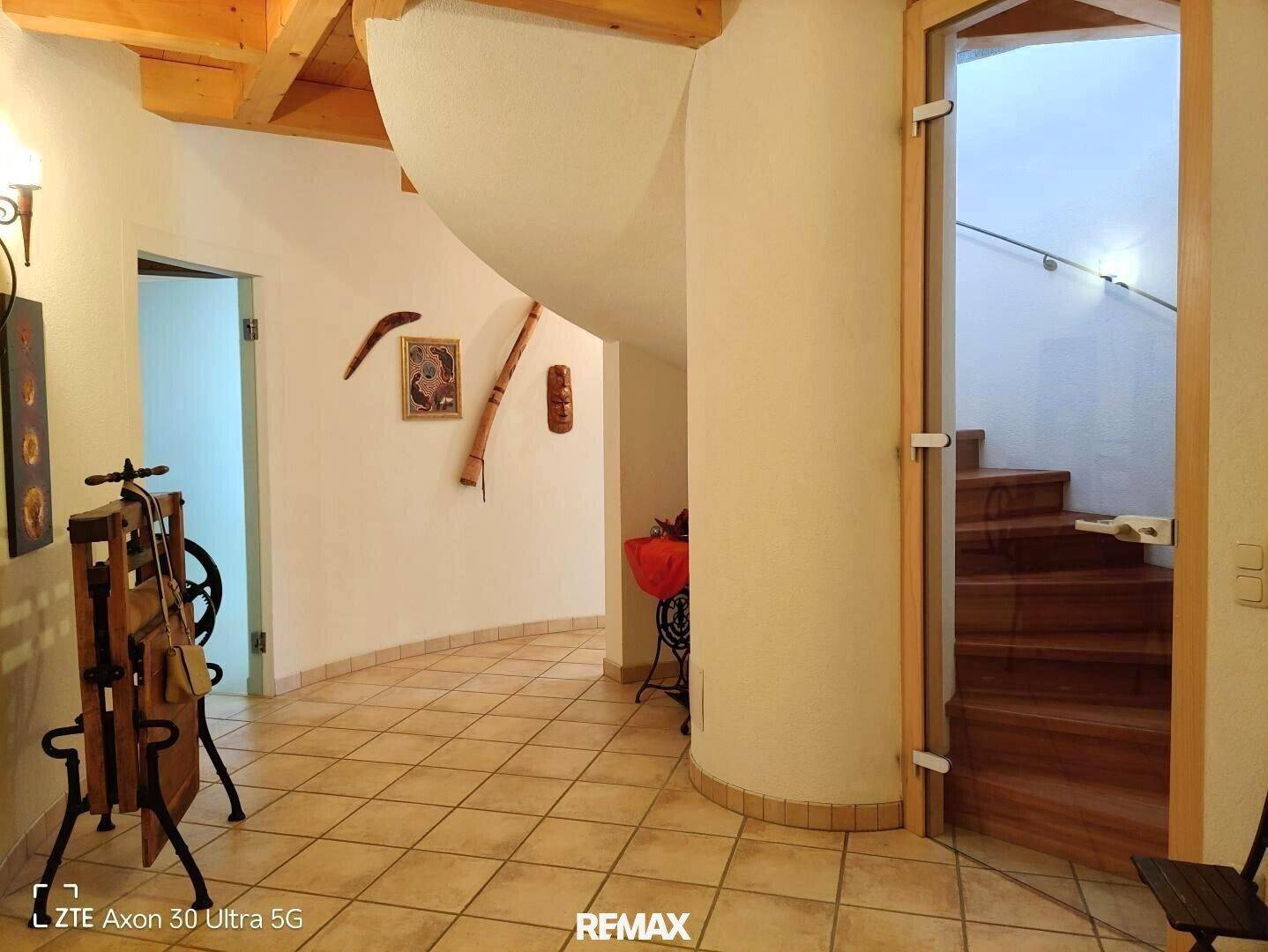 Heller Flur mit geschwungener Wand und einer eleganten Holzwendeltreppe, die das Obergeschoss verbindet.