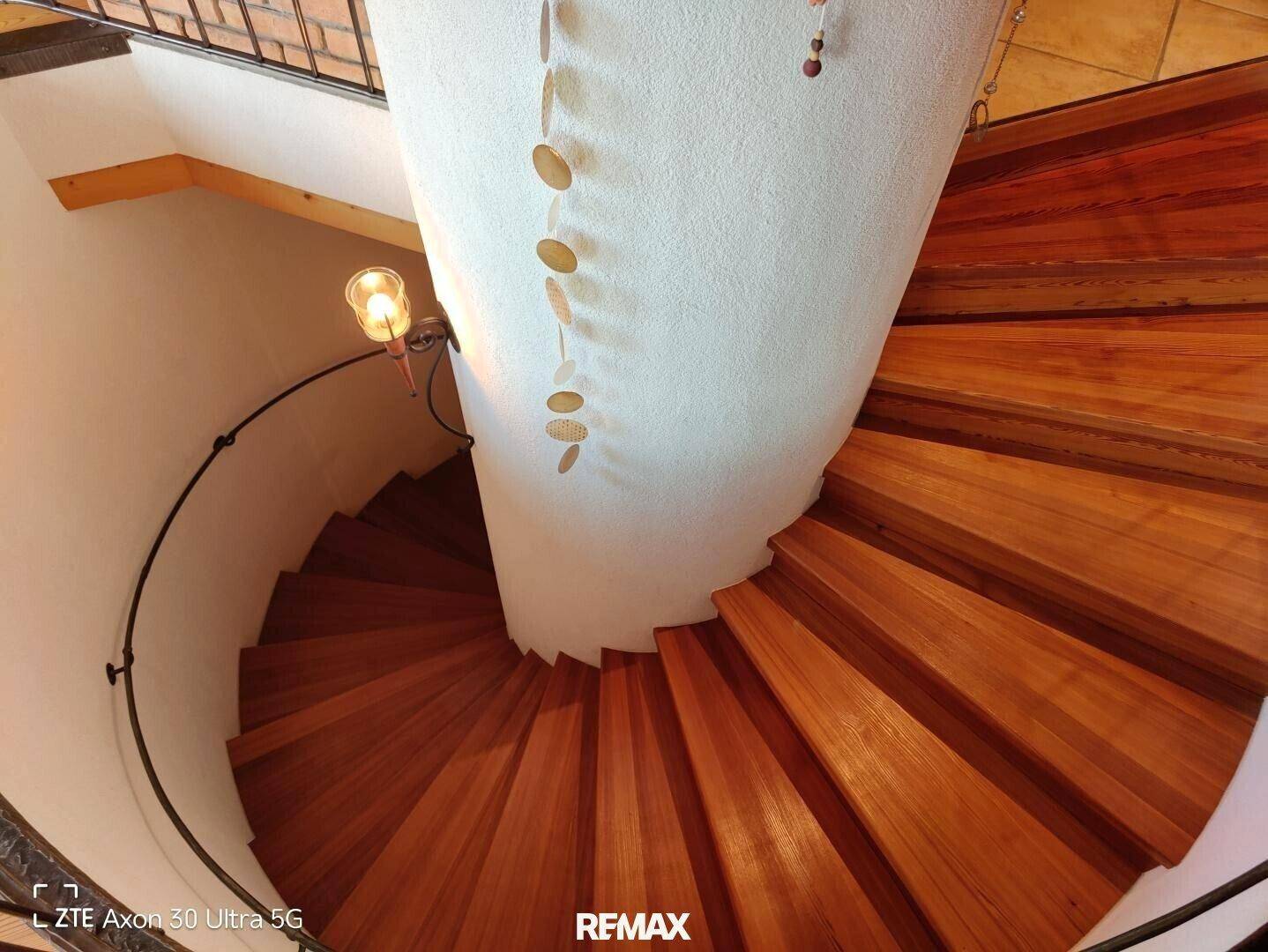 Elegante Holzwendeltreppe mit schmiedeeisernem Geländer, die die verschiedenen Etagen stilvoll verbindet.
