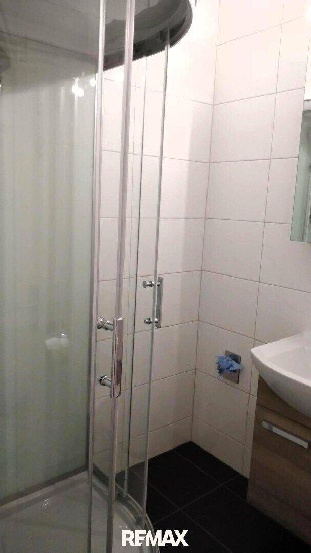 Duschkabine mit Glaswänden in einem hell gefliesten Badezimmer.