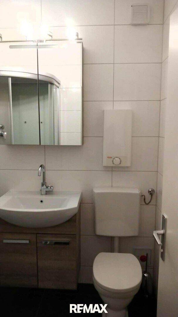 Badezimmer mit WC, Waschbecken und Spiegelschrank, hell gefliest.