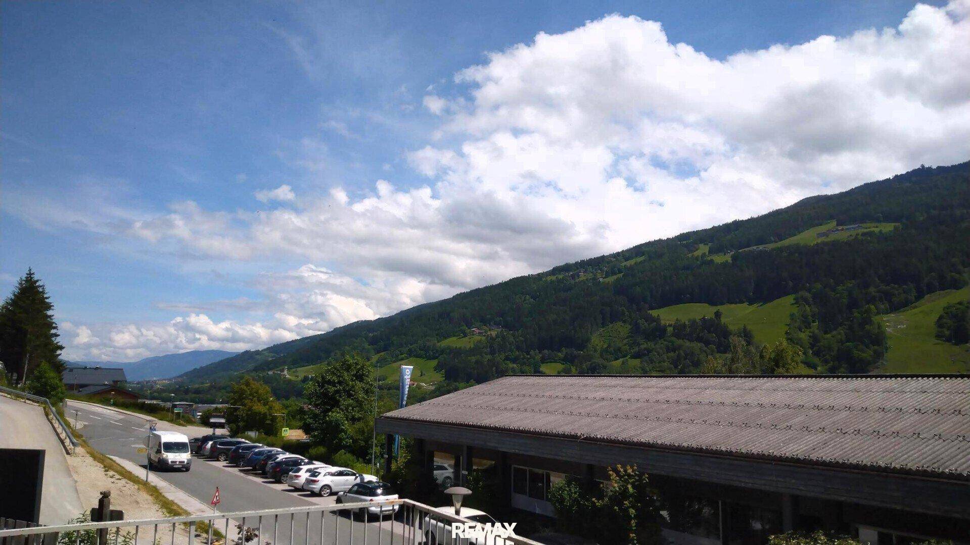Panoramablick auf die umliegende Berglandschaft mit einer Straße und parkenden Autos.
