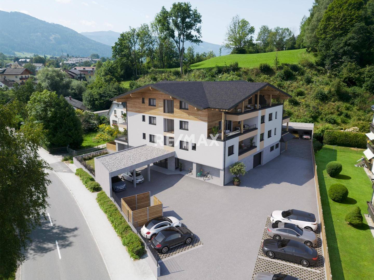 Modernes Mehrfamilienhaus in alpiner Umgebung mit Holzfassade, Carport und Parkplätzen.