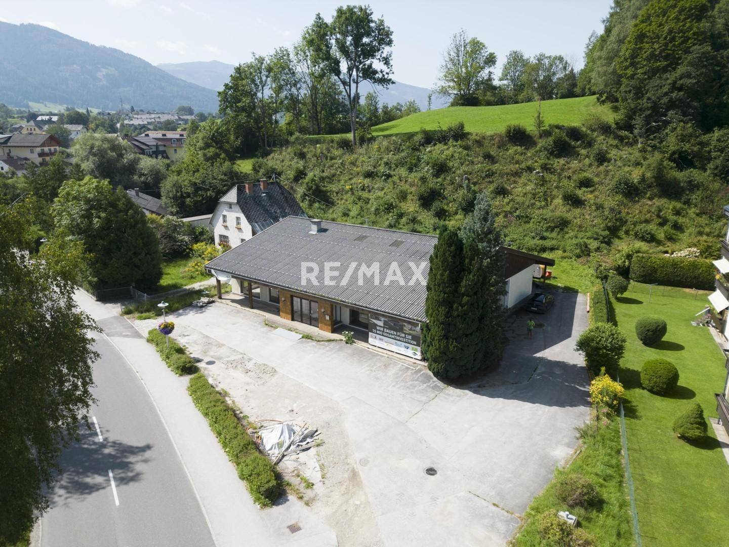 Luftaufnahme eines Gebäudes mit großem Parkplatz in einer grünen, bergigen Landschaft.