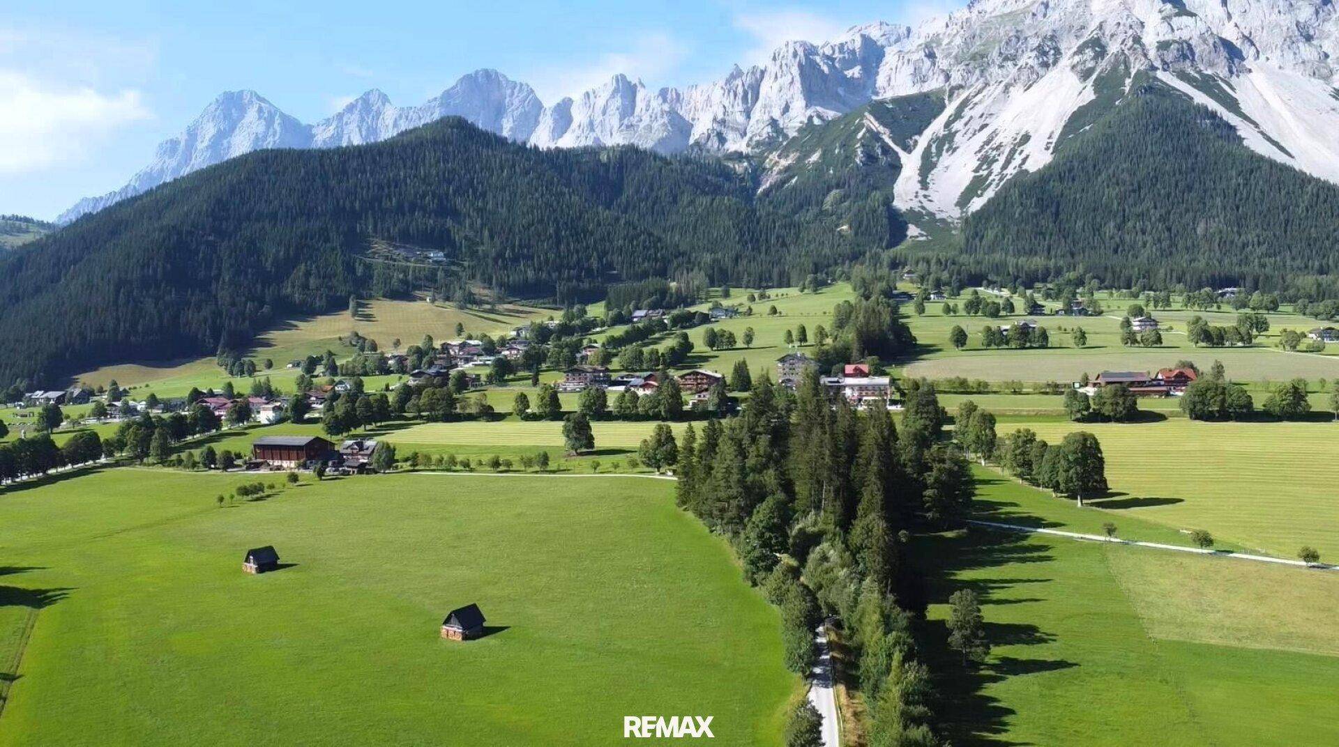 Weitläufige Berglandschaft mit grünen Wiesen und Wäldern, umgeben von majestätischen Gipfeln.