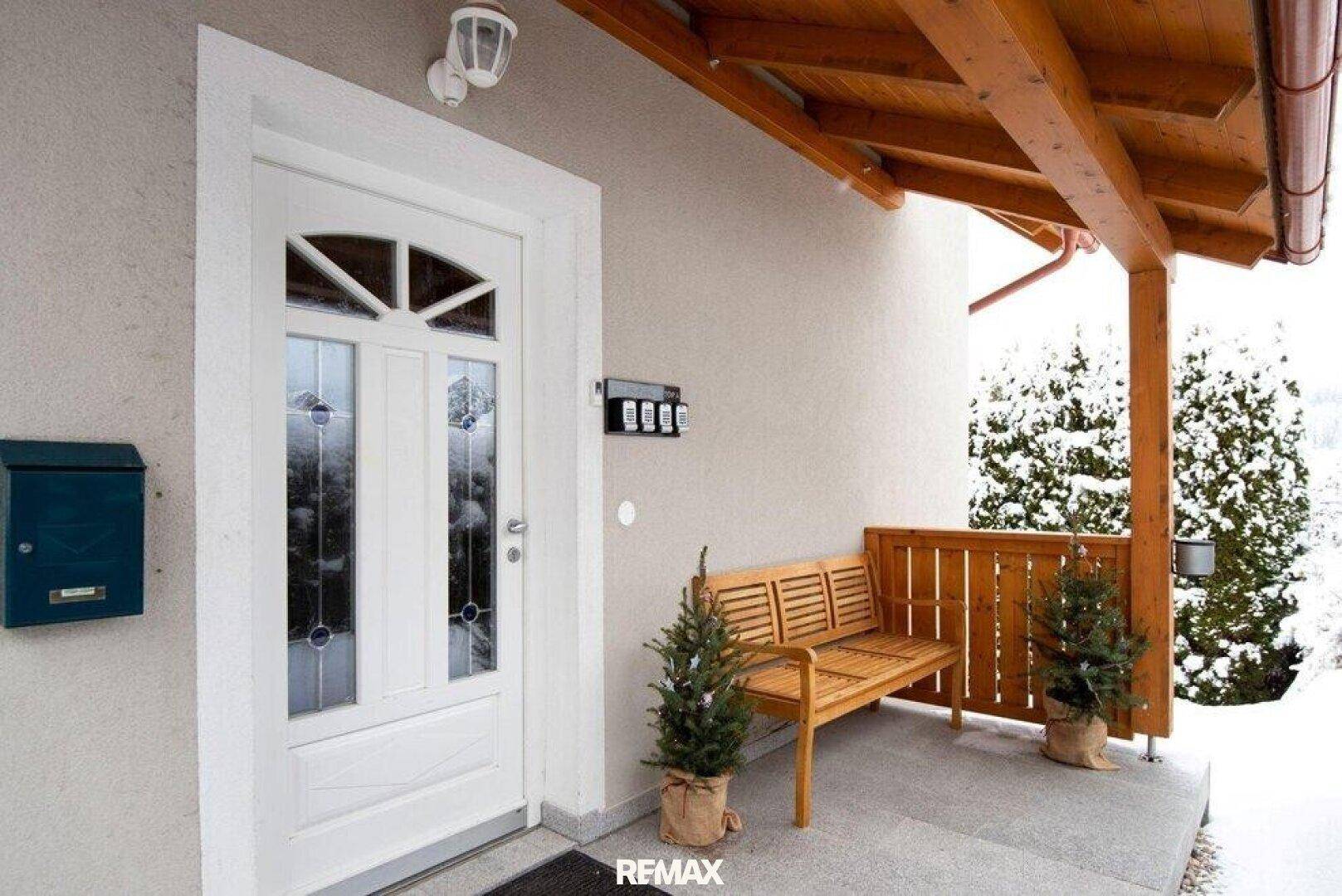 Eingangsbereich des Hauses mit Holzdach, Sitzbank und winterlicher Dekoration.