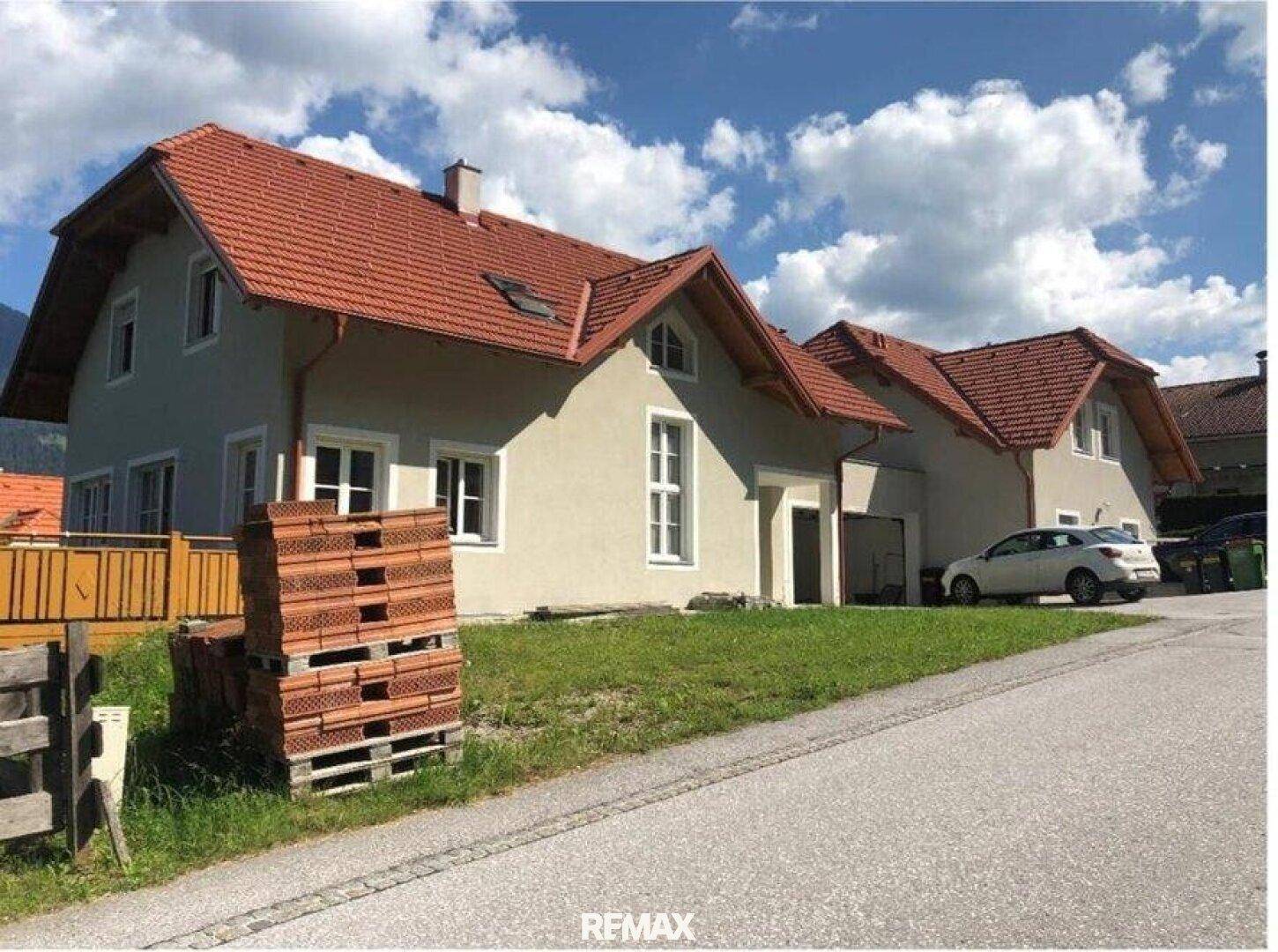 Zweifamilienhaus mit rotem Ziegeldach und heller Fassade in ländlicher Umgebung.