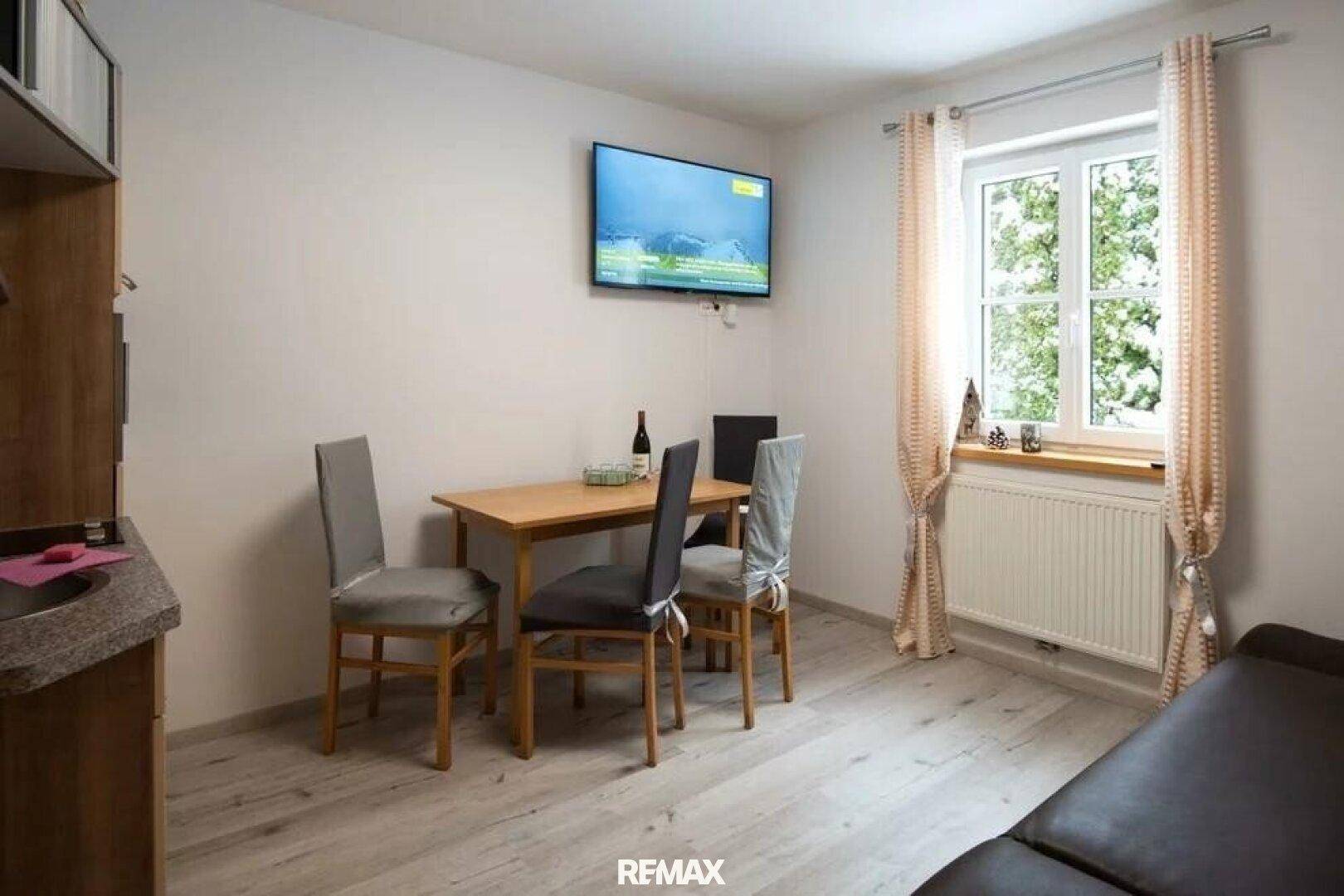 Heller Essbereich mit Fernseher und Fenster, ausgestattet mit einem Holztisch und Stühlen.