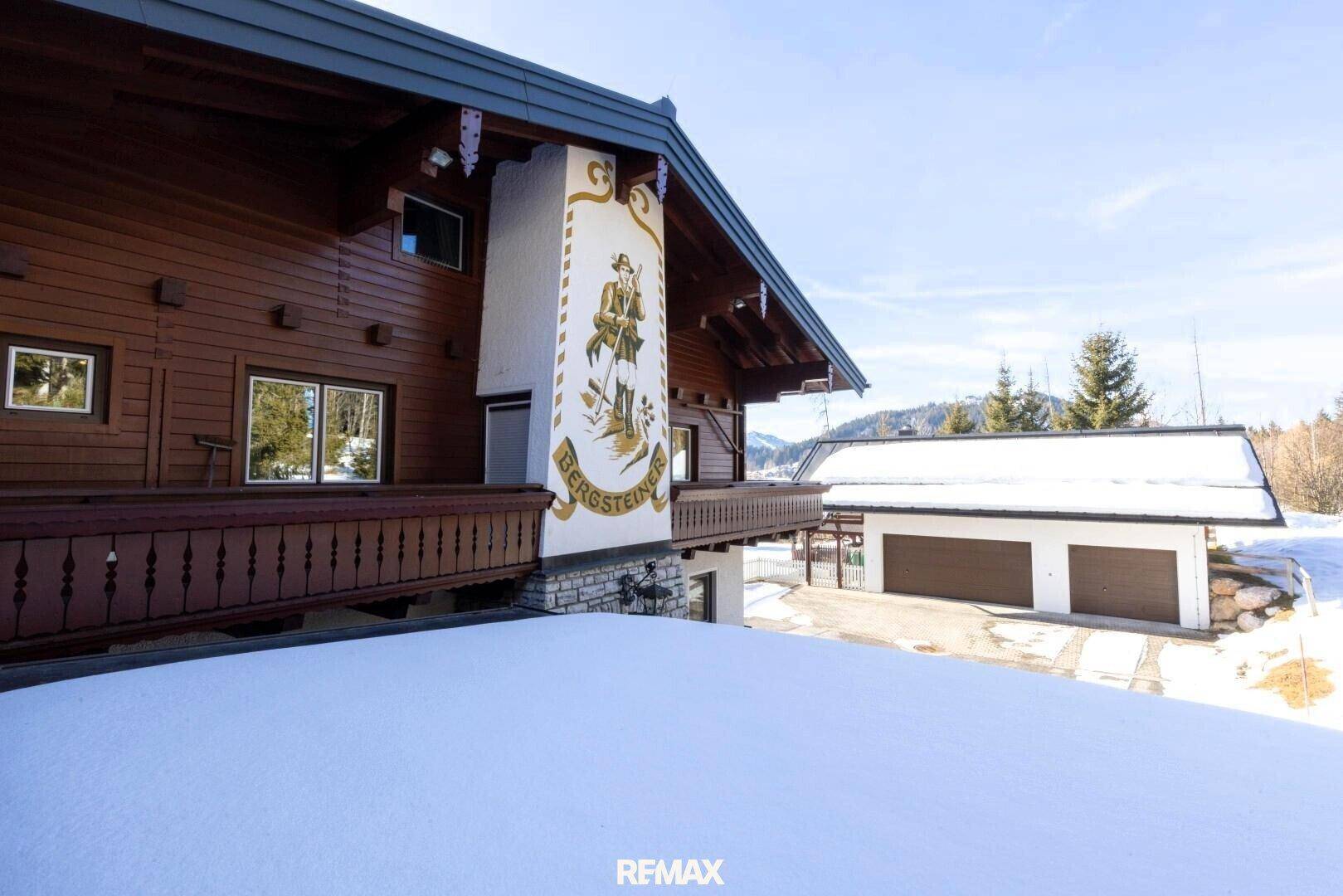 Detailansicht der Hausfassade mit traditioneller alpiner Malerei und einem Holzbalkon im Winter.