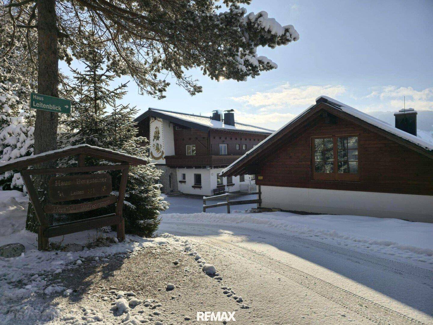 Winterlicher Eingangsbereich des Anwesens mit Holzschild und verschneiter Zufahrt zum Haus.