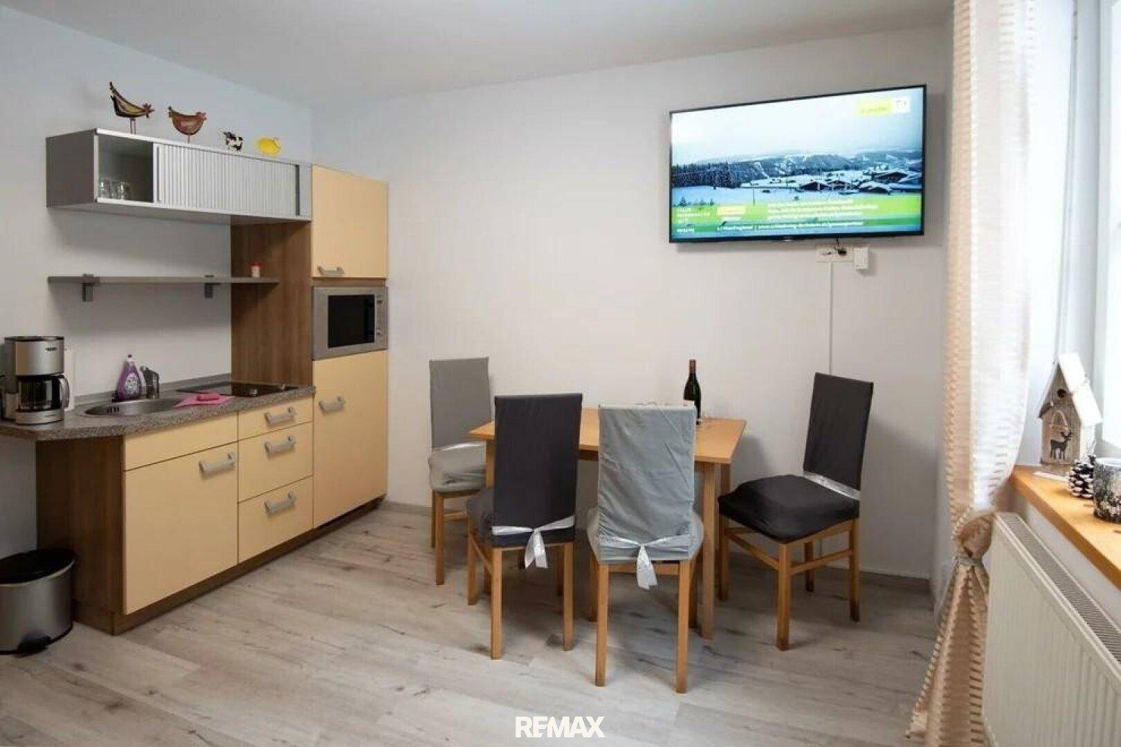 Heller Wohn-Essbereich mit kleiner Küchenzeile, Esstisch und Fernseher.