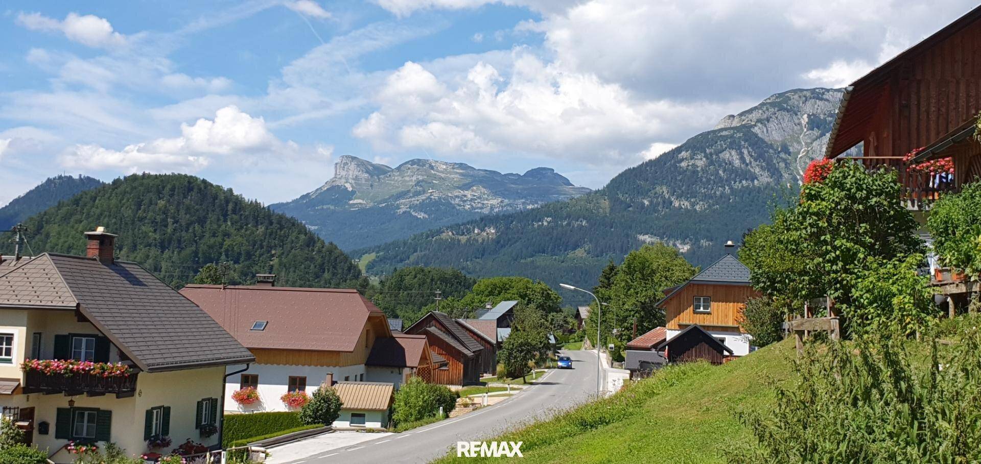 Charmante Häuser entlang einer Dorfstraße mit beeindruckendem Bergpanorama im Hintergrund.
