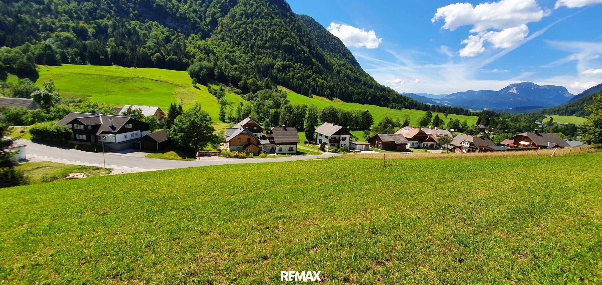 Idyllisches Dorf in einem grünen Tal, umgeben von Bergen und weiten Wiesenflächen.