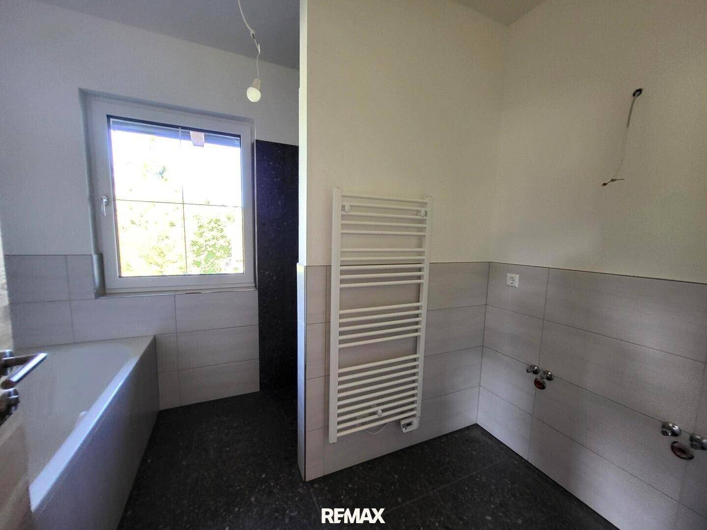 Helles Badezimmer mit Fenster, vorbereitet für Badewanne und Dusche, mit Handtuchheizkörper.