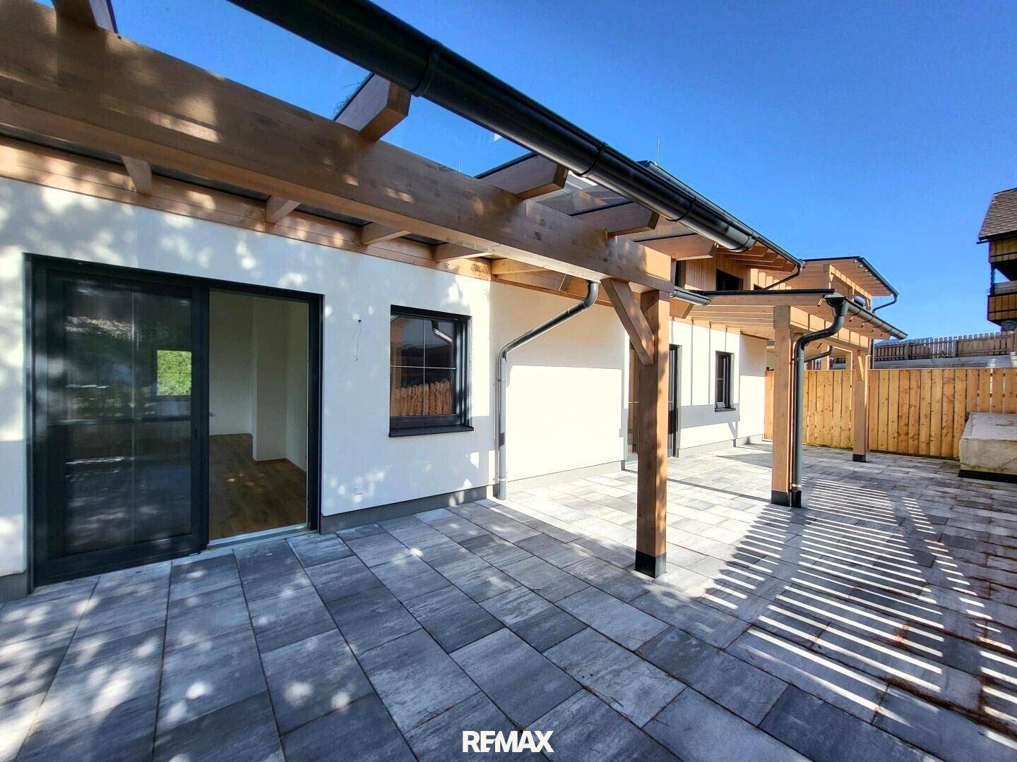 Überdachte Terrasse mit Holzbalken und Zugang zu einem hellen Innenraum.