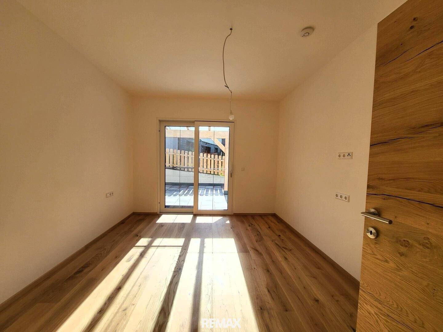 Geräumiges Zimmer mit Holzboden und Schiebetür, die Zugang zur Terrasse bietet.